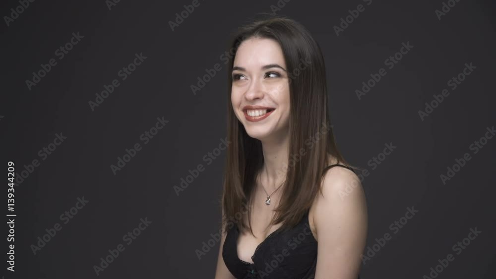 Young brunette woman in black underwear smiling and waving hand against gray background Young brunette woman in black underwear smiling and waving hand against gray background