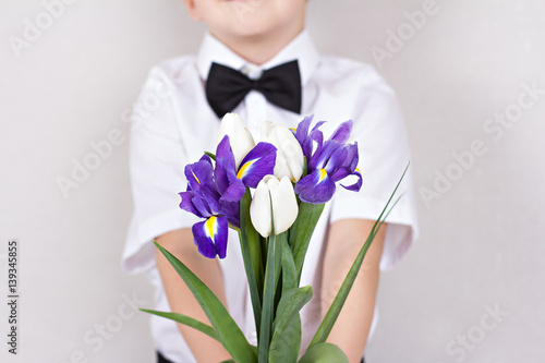 Bouquet of spring flowers in children's hands. Tulips, irises - early spring flowers is holding child. Greetings from the boy in smart clothes. Mother's Day, Women's Day, agift, a bouquet of flowers. photo