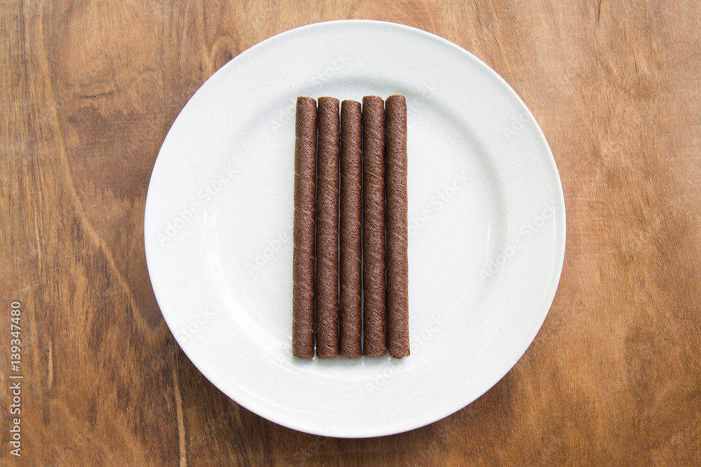 wafer rolls with chocolate in white plate on wooden table. wafer rolls with chocolate in white plate on wooden table.