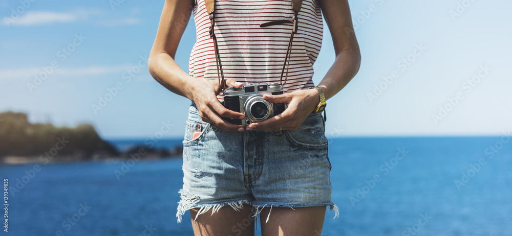 Tourist traveler photographer making pictures seascape on vintage photo camera on background yacht and boat piar, hipster girl enjoying peak mountain and nature holiday, ocean waves view - obrazy, fototapety, plakaty 