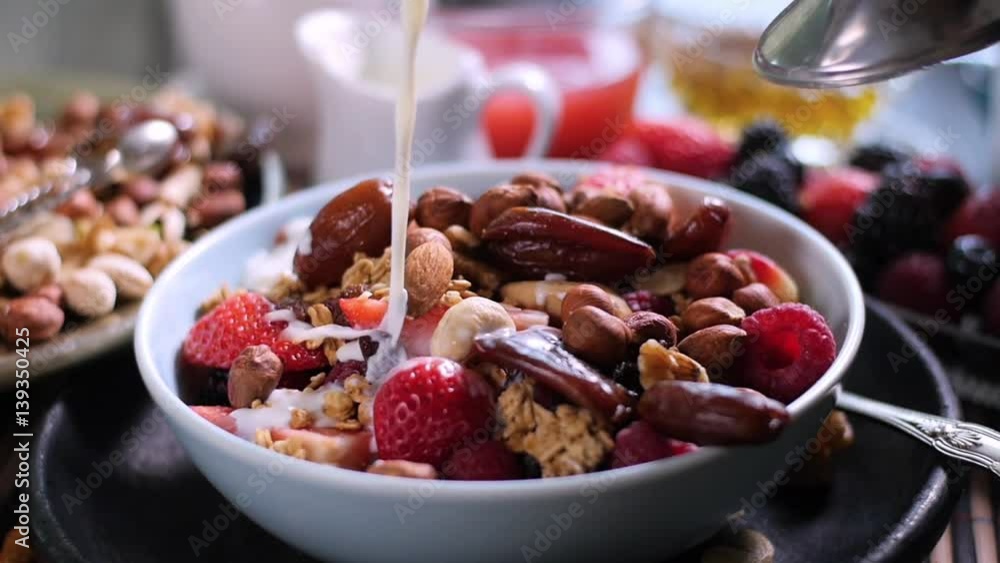 Slow motion: Pouring milk over a breakfast of cereals with berries, dry fruits and milk Slow motion: Pouring milk over a breakfast of cereals with berries, dry fruits and milk