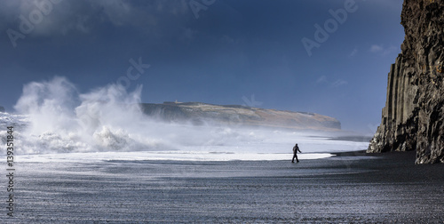 Man walking on Vik black beach, looking at giant waves - breathtaking Iceland in winter - amazing landscapes, storms and blizzards - photographers paradise