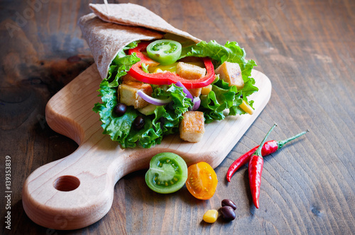 Tortilla wrap or burrito with tofu, greens, and vegetables, vegetarian healthy food, toned image