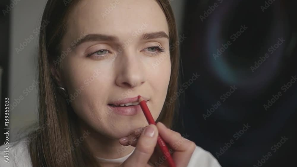 Beautiful attractive girl makes herself makeup, red pencil encircles the contour of the lips, slow motion Beautiful attractive girl makes herself makeup, red pencil encircles the contour of the lips, slow motion