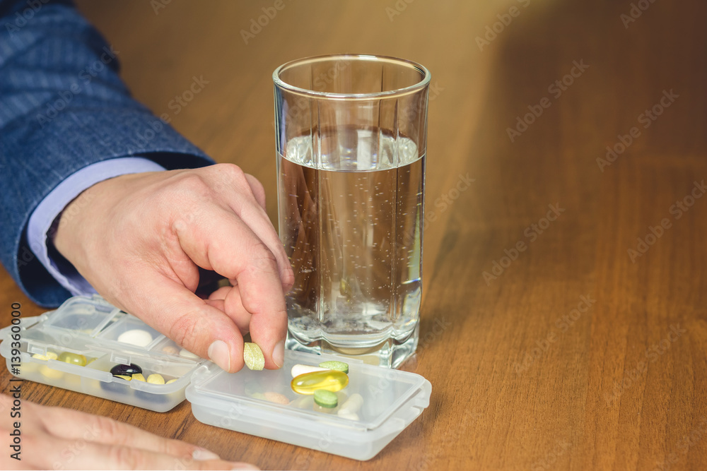 Glass of water, vitamins and nutritional, dietary supplement pills holding in hand of business man on work place. Glass of water, vitamins and nutritional, dietary supplement pills holding in hand of business man on work place.