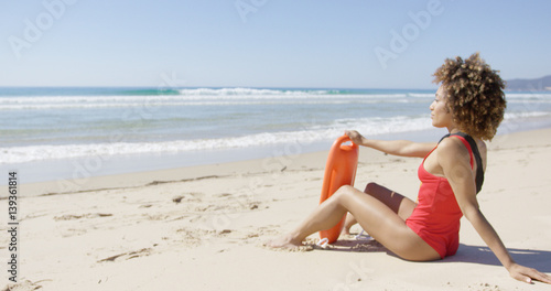 Female wearing red swimsuit with rescue float on beach looking into distance. Tarifa beach. Provincia Cadiz. Spain. 