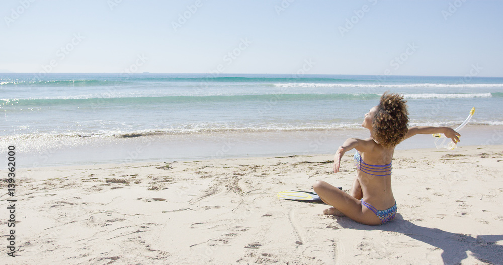 Female wearing two-piece swimsuit sitting with arms outstretched to sides on beach. Tarifa beach. Provincia Cadiz. Spain. Female wearing two-piece swimsuit sitting with arms outstretched to sides on beach. Tarifa beach. Provincia Cadiz. Spain.