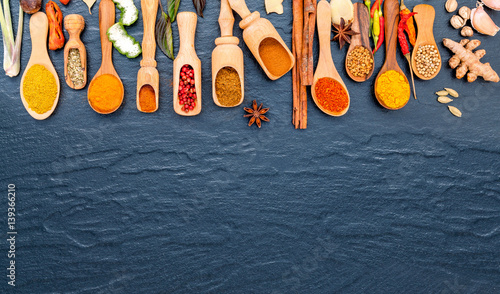 Various of Indian spices and herbs in wooden spoons. Flat lay of spices ingredients chilli ,pepper, garlic,dries thyme, cinnamon,star anise, nutmeg,rosemary and kaffir lime on the black stone.