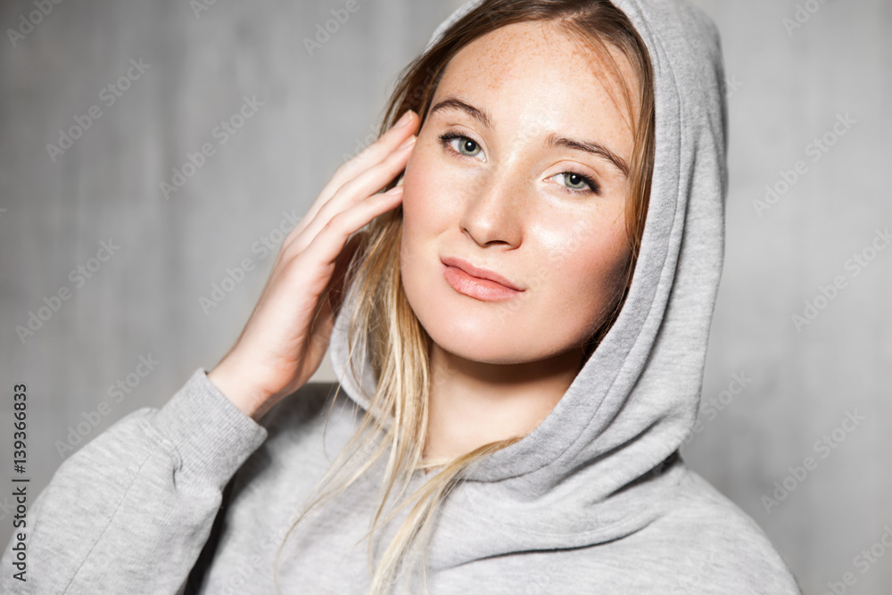 Portrait of young naturally beautiful woman in a gray sweatshirt on the cement wall background Portrait of young naturally beautiful woman in a gray sweatshirt on the cement wall background
