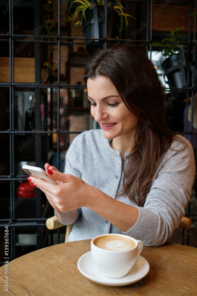 Beautiful girl sitting at a table in the cafe and use a smartphone Beautiful girl sitting at a table in the cafe and use a smartphone