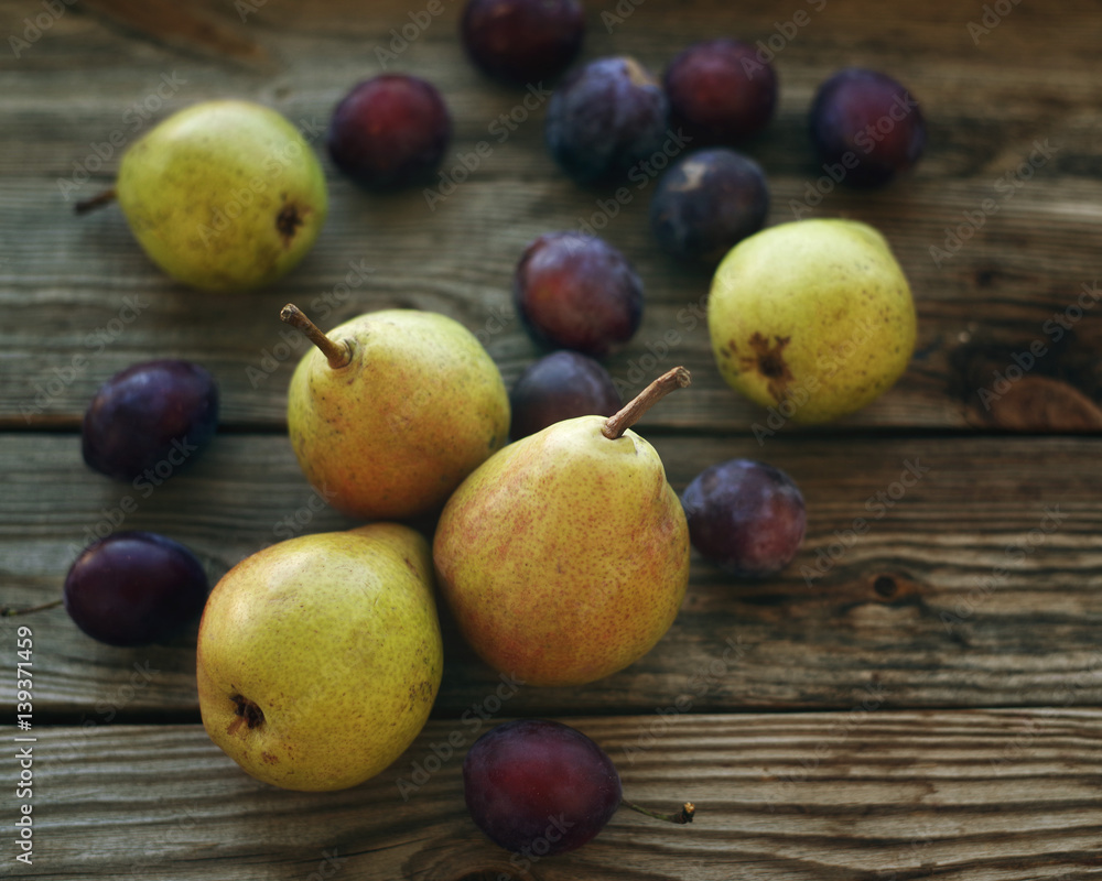 Ripe fresh pears and plums in a bowl on a wooden background close up. Autumn harvest of fruit. Ripe fresh pears and plums in a bowl on a wooden background close up. Autumn harvest of fruit.