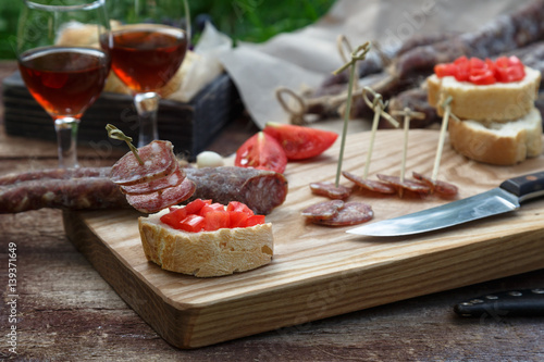 Bread, sausage, red wine, glass, cutting board and knife arranged on a wooden table for a snack in the countryside. photo