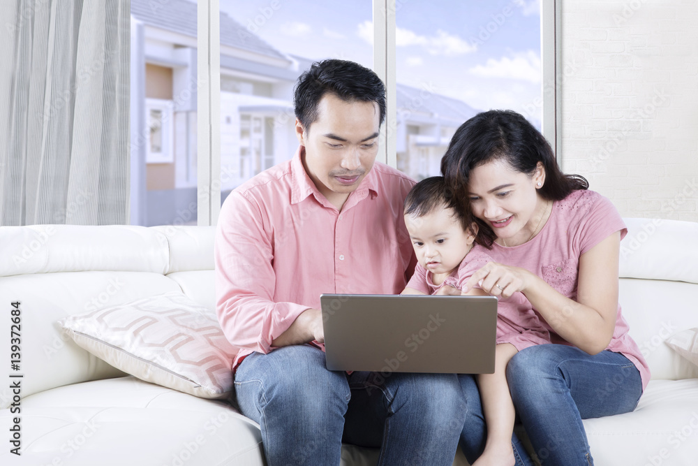 Fototapeta premium Asian family sitting on couch with laptop