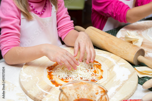 little girl in chefs hat is cooking pizza