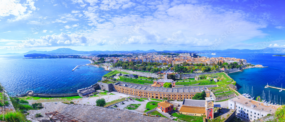Beautiful summertime panoramic aerial landscape. View of the ancient town on peninsula in to the crystal clear azure sea from Old Fortress of Corfu Town. Kerkyra - capital of Corfu island. Greece.