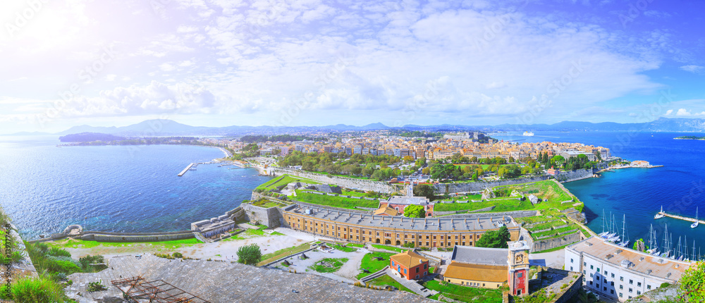 Beautiful summertime panoramic aerial landscape. View of the ancient town on peninsula in to the crystal clear azure sea from Old Fortress of Corfu Town. Kerkyra - capital of Corfu island. Greece.