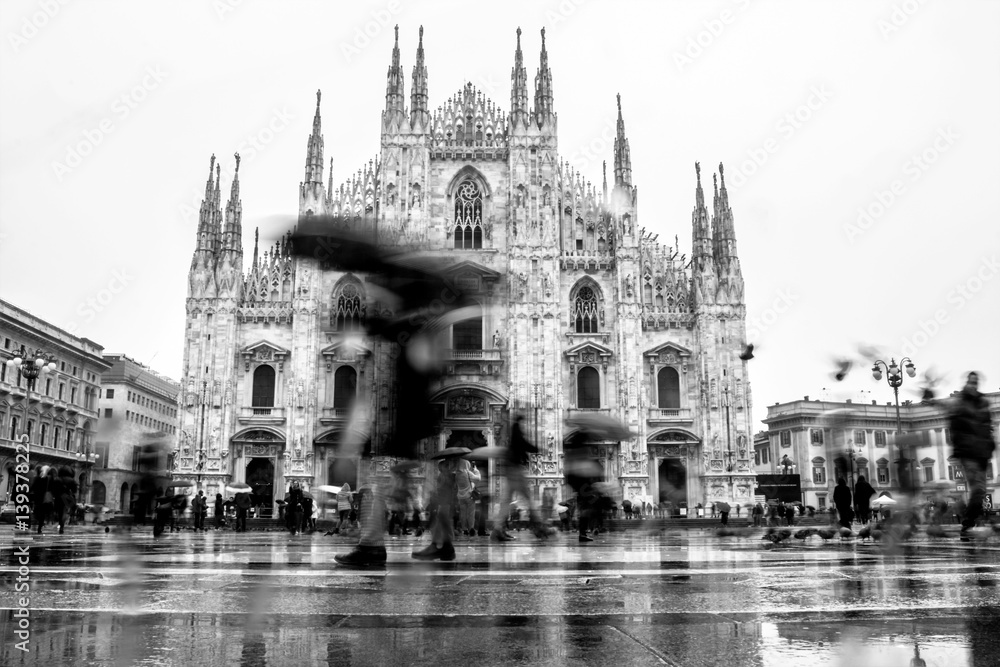 Milan (Milano), Italy - February 19, 2017: People silhouette under umbrellas in the Piazza Duomo square in front of Milan Cathedral church (Duomo) on rainy day - black and white version