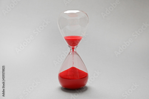 Hourglass with red sand on light background