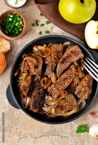 Fried liver with onions and apples on a concrete background