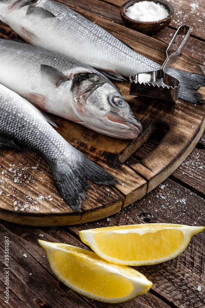fresh raw sea bass fish on wooden cutting board cooking concept on a dark wooden background top view