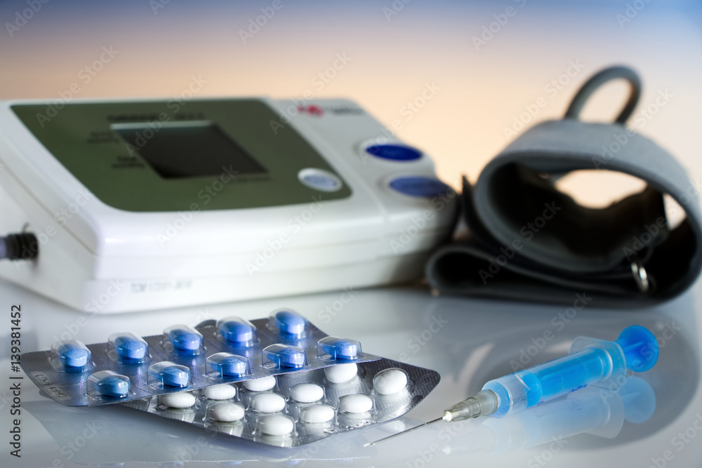 Medical pills and syringe against hypertension, equipment for measuring blood pressure in the background, drugs tray Medical pills and syringe against hypertension, equipment for measuring blood pressure in the background, drugs tray