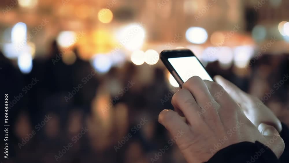 A young man is commuting to work while browsing his cellphone on a busy urban street at night. A young man is commuting to work while browsing his cellphone on a busy urban street at night.