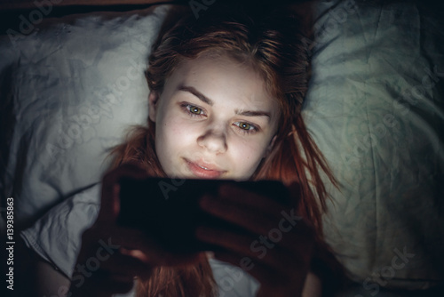 happy woman lies in bed and looks into phone