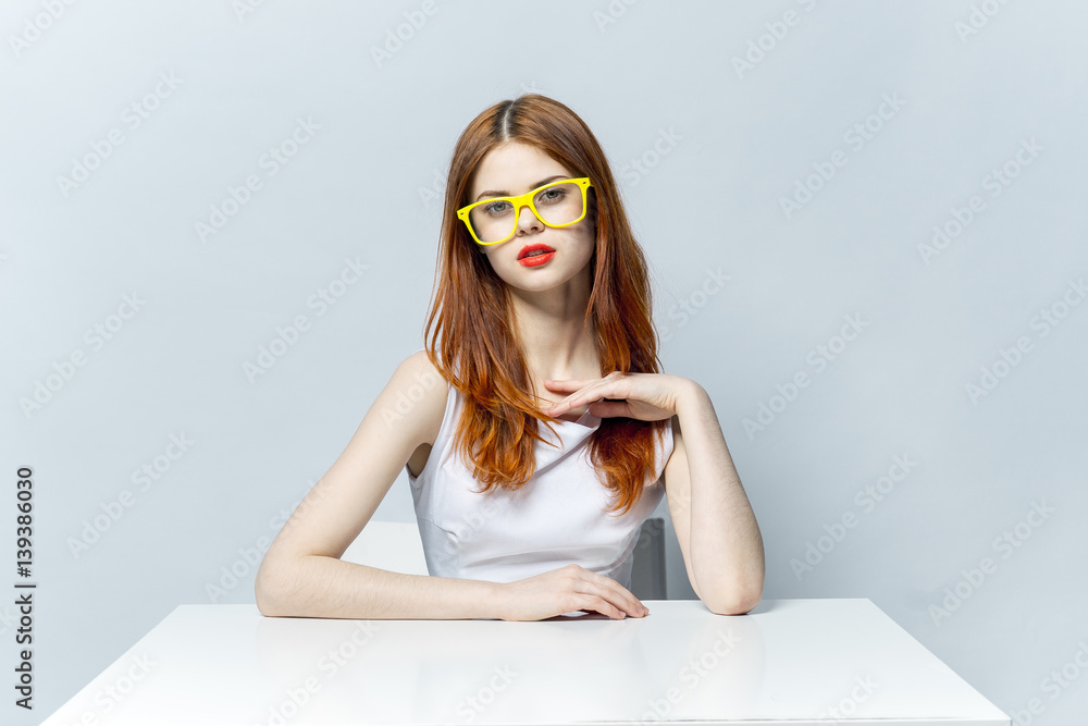 attractive woman in yellow glasses and with red lips sits at the table attractive woman in yellow glasses and with red lips sits at the table