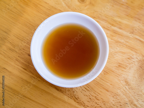 Chinese black vinegar sauce or sour sauce in a small white sauce cup on a wood table background. Dipping sauce for dimsum or dumpling or chinese food.