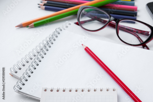 Red pencil on a white notepad and a number of glasses and pencils