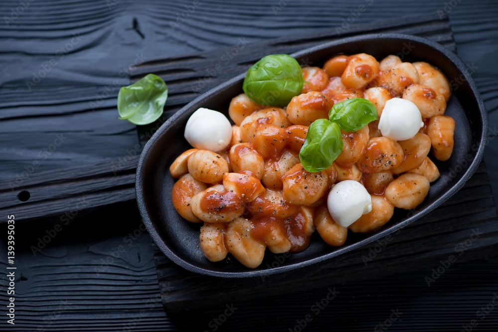 Cast-iron frying pan with potato gnocchi alla Sorrentina on a black wooden background Cast-iron frying pan with potato gnocchi alla Sorrentina on a black wooden background