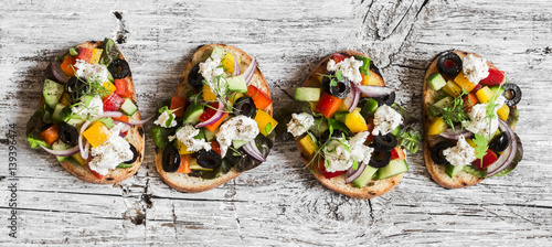 Greek salad style bruschetta on a wooden rustic board, top view. Delicious appetizers for wine or a snack