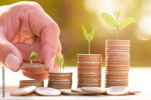 Close up of male hand stacking gold coins with green bokeh background ,Business Finance and Money concept,Save money for prepare in the future.Trees growing on coin photo