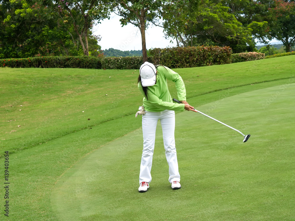 Fototapeta premium Smiling woman golf player putting successfully ball on green, ball dropping into cup,