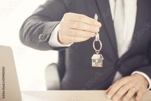 Estate agent giving house keys on a silver house shaped keychain