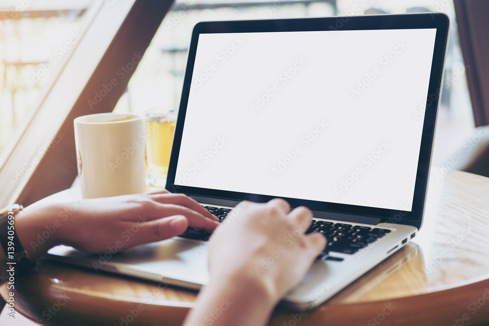 Mockup image of hands using laptop with blank white screen on vintage wooden table in cafe