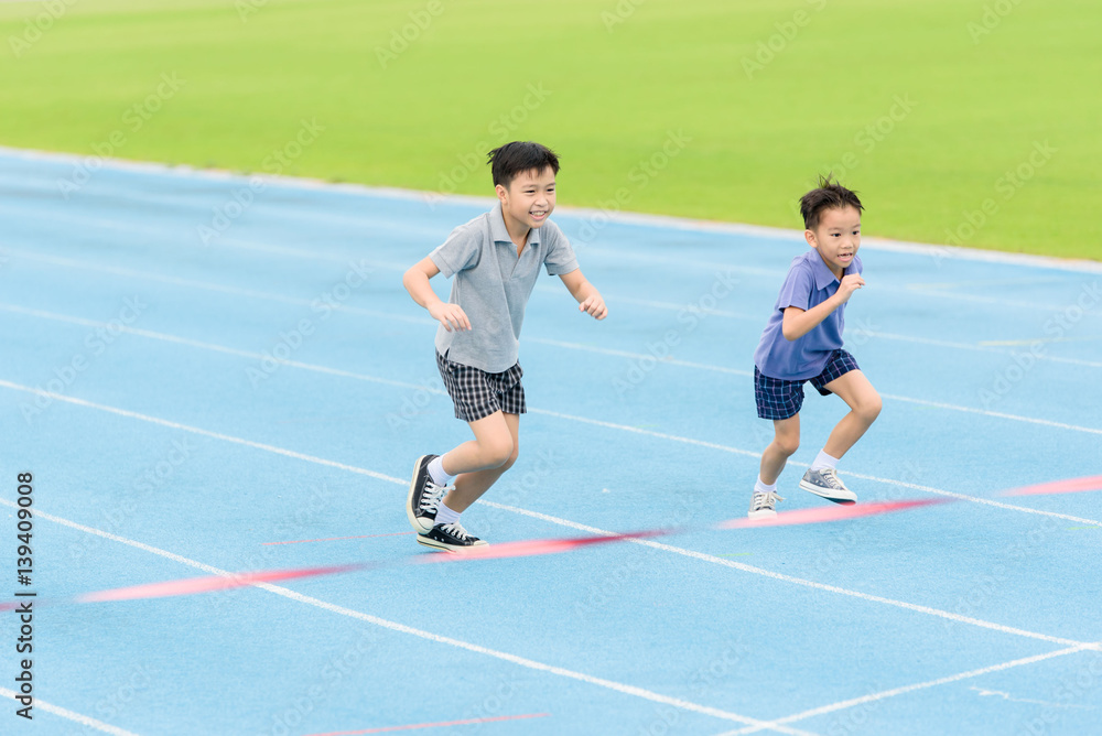 Obraz premium Young Asian boy running on blue track in the stadium