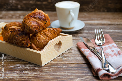 Freshly croissants  with cup of coffee and  cutlery on wooden try. Breakfast concept.