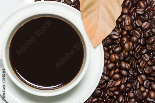 Black coffee in the cup and roasted coffee beans background.