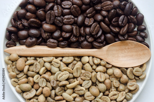 Raw and roasted coffee beans with wooden spoon.