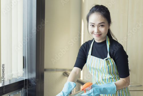 happy woman in gloves cleaning with cleanser spray at home
