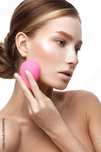 Young girl with a healthy skin and Nude makeup. Beautiful model on cosmetic procedures with a sponge to apply foundation. The beauty of the face.