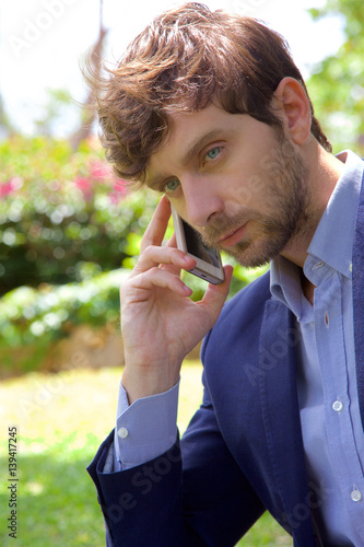 Serious business man on the phone while working with pc in park closeup