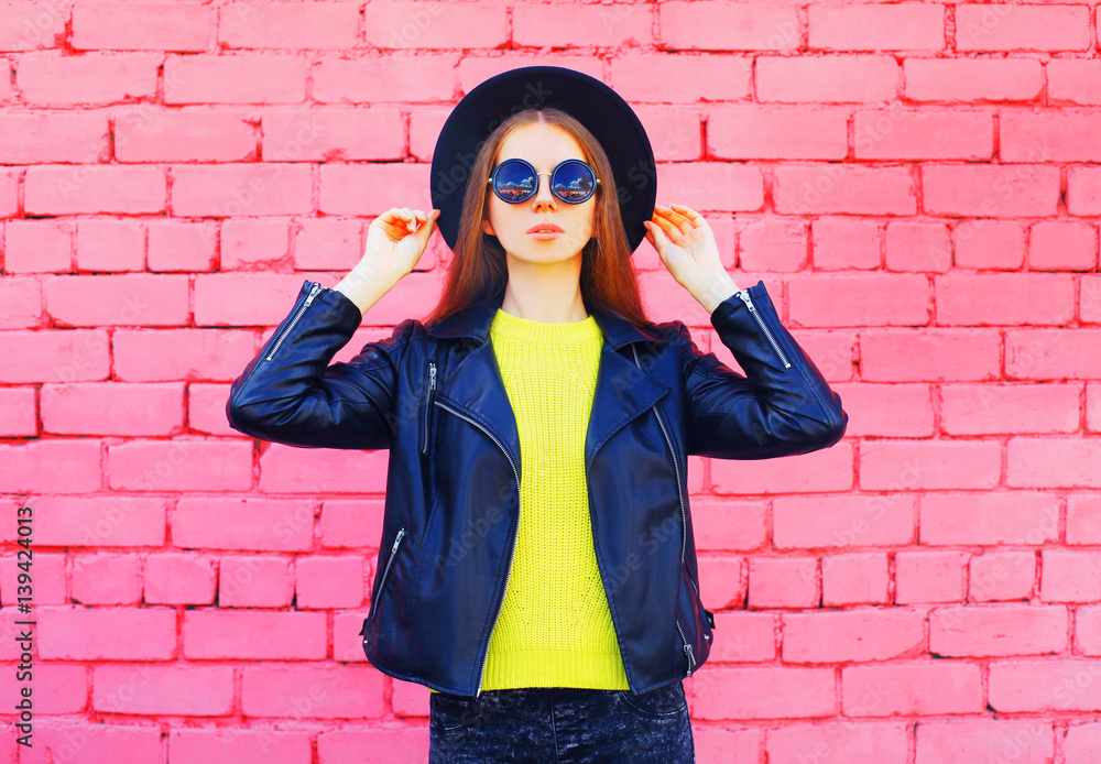 Fashion woman wearing a black hat and yellow knitted sweate rjacket over colorful pink bricks background Fashion woman wearing a black hat and yellow knitted sweate rjacket over colorful pink bricks background