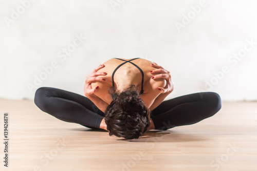Dancer doing advanced butterfly stretch exercise sitting leaning forward holding shoulders. Young flexible woman in beautiful sensual pose.