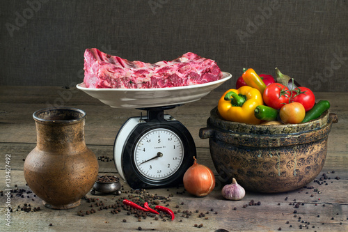 The meat on the scales, vegetables and pottery on a wooden table