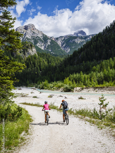Mountain biking woman and young girl along river in Dolomites, Italy