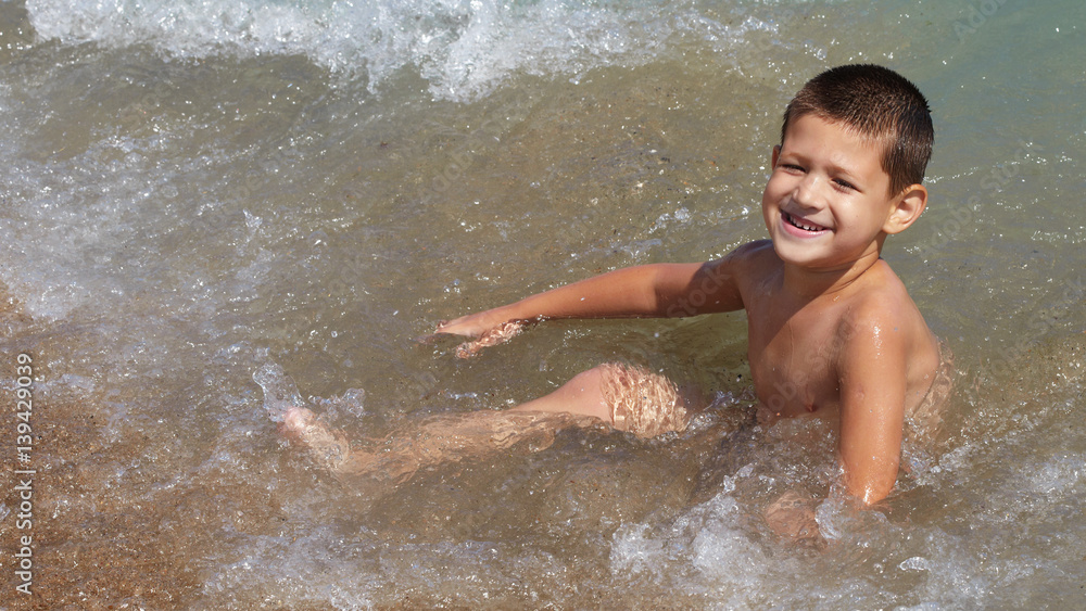 Fototapeta premium Little boy plays in the sea