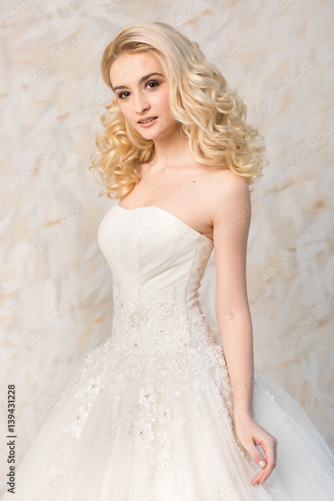 a gorgeous smiling blonde bride with beautiful curly hair in a white wedding dress on a light background. beautiful young model with bridal hairstyle and makeup in a white magnificent dress. a gorgeous smiling blonde bride with beautiful curly hair in a white wedding dress on a light background. beautiful young model with bridal hairstyle and makeup in a white magnificent dress.