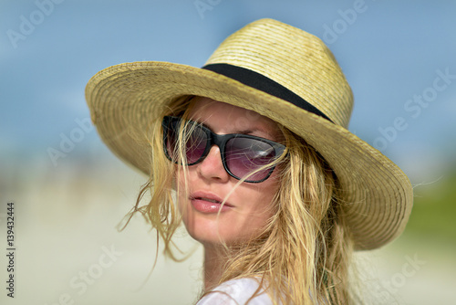 Beautiful young girl in the straw hat and sunglasses is smiling on the beach